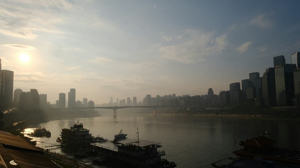 Sunrise over a foggy cityscape with boats on the river