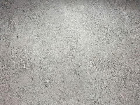 A light grey wall with a rough and uneven plaster texture