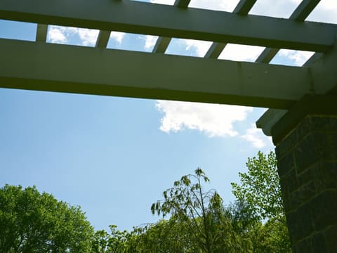 Sunny blue sky, white clouds, green trees, and a pergola