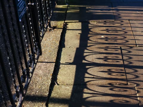 Wrought Iron Railings: shadows of ornate railing cast on stone walkway